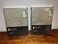 Two packages of beige textured floral pattern grommet curtains from Simons Maison, still sealed in plastic packaging.