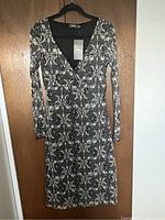 Front view of a new women's long sleeve black and white floral printed dress with tag, hanging on a hanger against a wooden door