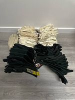 Photo showing 36 pairs of thick white cotton gloves stacked together and 14 pairs of black waterproof gloves grouped together on floor.