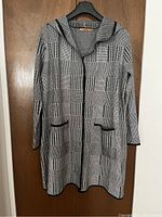 Front view of the long hooded sweater coat hanging showing checkered pattern, pockets, and hood.