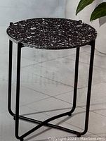 Full view of the round side table showing the black and white speckled stone top and the black metal frame base.