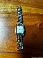Top view of the silver-tone Swiss Military ladies quartz wristwatch lying flat on wooden surface, showing rectangular white dial with black Arabic numerals, date window at 6 o'clock, and metal bracelet.