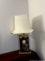 Full view of the decorative table lamp with cream fabric shade and rectangular black base with floral design.