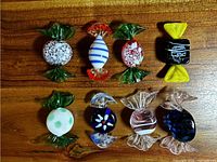Top view of all eight glass candy ornaments on a wooden surface, showing various colors and patterns