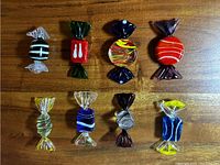 Top down view of all eight decorative glass candy figurines arranged in two rows on a wooden surface, showing varied colors and designs.