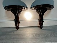 Pair of dark wood wall shelves showing front and side profiles with curved tops and turned decorative supports.