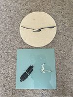 Full view of two art pieces on carpet: round sand sculpture and square painted glass art