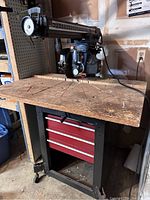 Full view of the Craftsman radial arm saw mounted on a wooden top attached to a metal cabinet with red drawers, showing the saw blade and work surface.