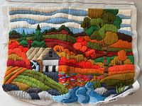 Full view of the unframed crewel embroidery showing the entire colorful countryside scene with house, trees, hills, pond, and sky.