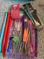 Top view of various knitting needles and tools in a striped box, showing different sizes and colors