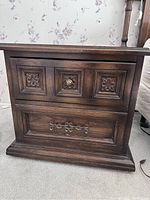 Front view of one dark brown wooden mid-century modern nightstand with two drawers, decorative carved panels, and metal hardware.