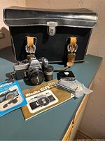 Wide shot showing Minolta SRT-101 camera with accessories including leather lens case, owner's manual, lens keeper accessories and black leather carrying case.