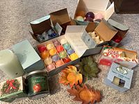 Photo showing multiple boxed tea lights, colorful spherical votive candles, a large green pillar candle labeled Cucumber Mint, holiday-themed Yankee Candle votives, and three autumnal leaf votive holders.