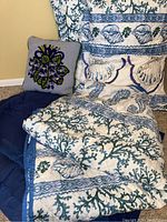Photo of the folded queen quilt, two matching shams, navy blanket and crewel work floral pillow showing details of fabric and pattern