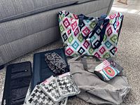 Eight assorted Thirty-One bags including colorful pattern tote, gray tote, small pouches, and organizer bag on carpet by couch.