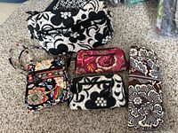 Top down view showing all five items arranged on carpet: one large handbag, one smaller crossbody bag, two wallets, and one knitting needle holder.