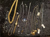 Overview of all vintage jewelry items laid out on black fabric including necklaces, chains, watch, and pins.