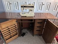 Singer 1425n sewing machine mounted open on top of the motorized wooden cabinet with both cabinet doors open revealing storage compartments and drawers.