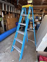 Full view of a blue Werner fiberglass ladder standing in a garage, showing its structure and six steps.