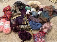 Lot of assorted yarn skeins and balls along with finished and unfinished scarves on carpeted floor.