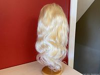 View of blonde wavy wig on stand showing natural waves and length.