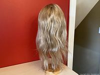 Back view of long wavy dirty blonde lace front wig on a wig stand, showing length and waves.