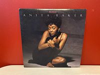Front view of the Anita Baker Rapture vinyl album cover, featuring a photo of Anita Baker dressed in black sitting against a dark backdrop.