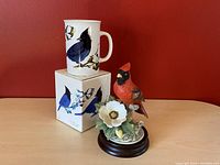 Porcelain cardinal bird figurine on wooden base next to Bradshaw Stellers Jays mug on matching box, showing overall lot items.