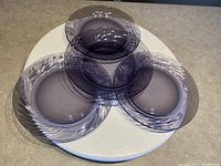 Four vintage Pyrex Corelle Coordinates Festiva Amethyst glass plates arranged on a white surface. Plates have a purple swirl pattern with solid purple centers.