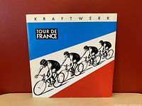 Front view of Kraftwerk Tour De France album cover featuring the cycling design with blue, white, and red colors.