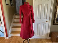 Mannequin displaying long red wool coat with belt, showing full length and collar