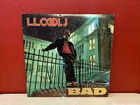 Close-up of album cover showing L.L. Cool J posing by a fence and building with album title BAD.