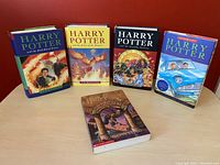 Five Harry Potter books displayed upright and one softcover book lying flat on table, showcasing colorful dust jackets and illustrations.
