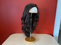 Wig displayed on a mannequin head with a wooden stand, showing the long, dark brunette, wavy synthetic hair.