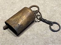 Close up of primitive blacksmith cowbell with attached rings and leather strap, showing the worn patina and rustic condition.