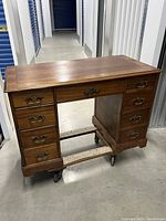 Front view of antique wooden desk showing seven drawers and caster wheels