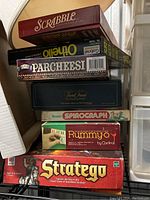 Stack of classic board games including Scrabble, Othello, Parcheesi, Trivial Pursuit, Spirograph, Rummy-O, and Stratego boxes.