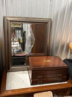 Image of wooden jewelry box on surface in front of large framed mirror.