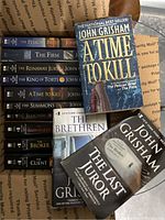 Stack of 11 John Grisham paperback novels showing spines and front covers of main titles.