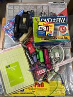 Overhead view showing assortment of office supplies including discs, tape dispensers, stapler, pencil sharpener, cables, and legal pads