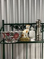 Photo showing four items on a metal shelf including decorative bowl, cat figurine, white pineapple decor, and pepper grinder