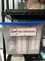 Plastic bin labeled 'NO SMOKING' filled with individually packaged no smoking signs.
