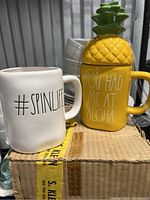 Photo showing side view of both mugs: white '#SpinLife' and yellow pineapple-shaped 'You Had Me At Aloha'.