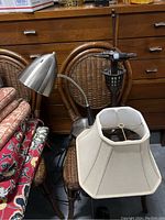 Desk lamp with metal conical shade, flexible neck, and round metal base placed on a chair with woven rattan backrest.