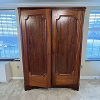 Wood armoire closed showing paneled double doors and curved edges.