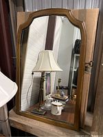 Front view of the wood framed mirror showing the curved top design and reflective glass surface with some smudges and dust. The mirror is positioned on top of cardboard backing and reflected objects are visible.