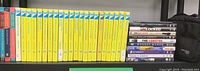 Photo of 22 Nancy Drew books with yellow spines, additional 5 books with darker spines, stack of 12 DVD movies with visible titles, black Case Logic carry case behind.