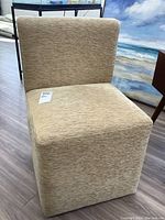 Front view of small beige upholstered accent chair on light wooden floor, showing its compact shape and textured fabric.