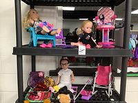 View of shelf with two dolls in outfits, small purses, stroller, and doll accessories.
