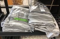 Two folded striped drapery panels, one packaged in plastic, placed on a black shelf.